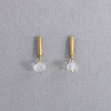 エシカルでサステナブルなジュエリーを提案するHASUNAのK18ブルームーンストーンのピアス。パーツ、金具はすべてK18製。長さ約1㎝、幅約1mm程度の三角柱のバー型パーツの先にワイヤーで留めたブルームーンストーンが下がり、揺れます。三角柱の裏面上部にポストが立っています。ブルームーンストーンは濁りが非常に少なく、ほの青いストーンに青い輝きが入る美しいもの。ストーンの大きさは幅約4.5mm程度、高さ3mmほどの角のない平たい円柱のような形。普段から着けやすいサイズ感です。エシカル エシカルジュエリー HASUNA サステナブルHASUNA