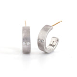 エシカルでサステナブルなジュエリーをご提案するHAUSNAのシルバー925製ダイヤモンドの留まるフープピアス。
直径約13mm、幅約4mm前後のCを描くようなフープ型のピアス。着けたときに正面に来るところに、直径約1mmのダイヤが2石並んで留まっています。シルバーの表面は細かなスクラッチでマット加工が施されています。C型の一番上にあたるところにK18製のピアスポストが立っています。耳たぶを包むようにCの形を描きます。
シルバー SV925 ピアス シルバーダイヤモンドピアス フープピアス ギフト プレゼント ダイヤモンドピアス ダイヤのピアス エシカル サステナブル エシカル ジュエリー ハスナ HASUNA